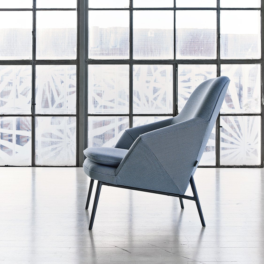 Light blue upholstered chair with a geometric design, paired with sleek dark legs, set against a bright window backdrop.