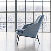 Light blue upholstered chair with a geometric design, paired with sleek dark legs, set against a bright window backdrop.