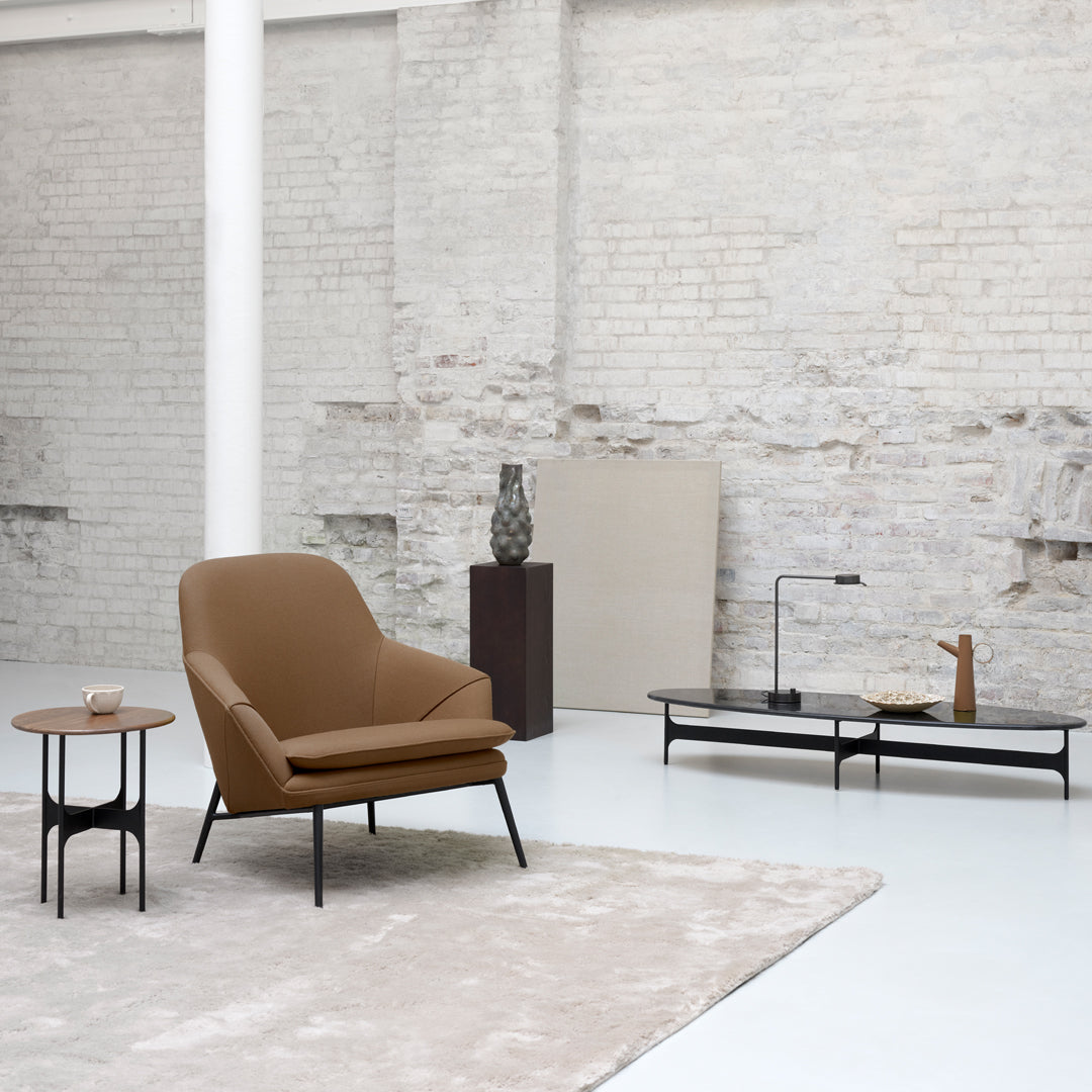 Brown upholstered chair and light beige accents on a textured rug, minimalist decor against a white brick backdrop.