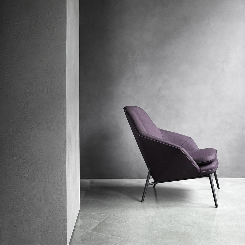 Modern purple accent chair against a minimalist gray wall and concrete floor, showcasing sleek design and subtle color contrast.