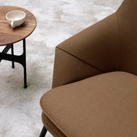 Brown upholstered armchair corner with minimalist wooden side table and white cup on textured light gray carpet.