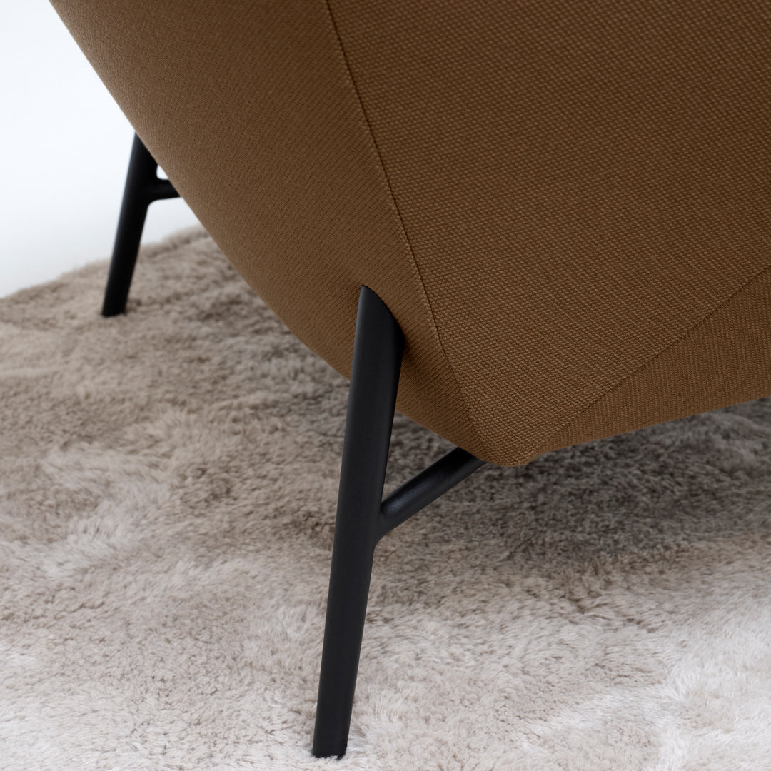 Brown upholstered chair with sleek black metal legs on a soft, light-colored rug. Modern, minimalistic design.