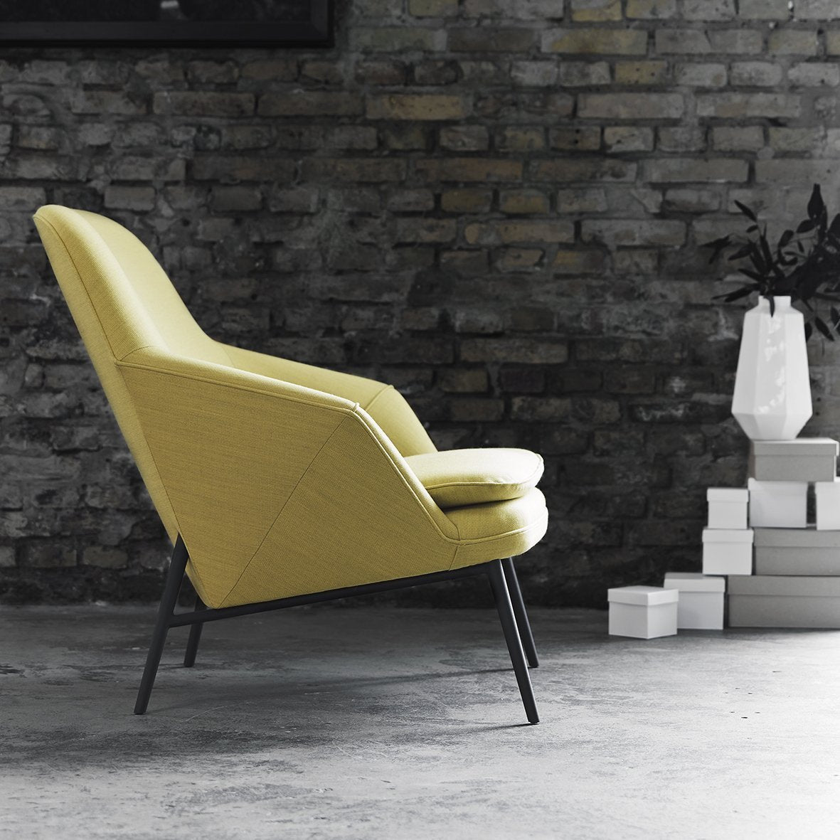 Yellow patterned chair with a sleek design, set against a dark brick wall. Modern, minimalist style.