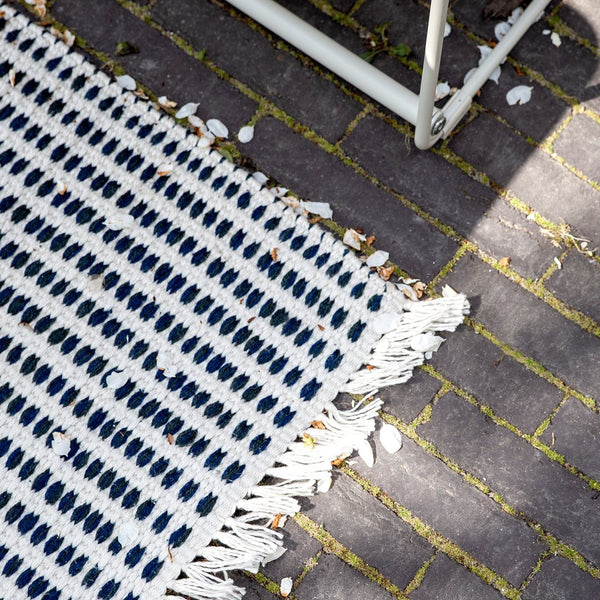 Navy and white striped woven rug with fringe, featuring a textured pattern and outdoor setting.