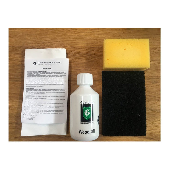 "White wood oil bottle, yellow sponge, black scrub pad on a light wooden surface."
