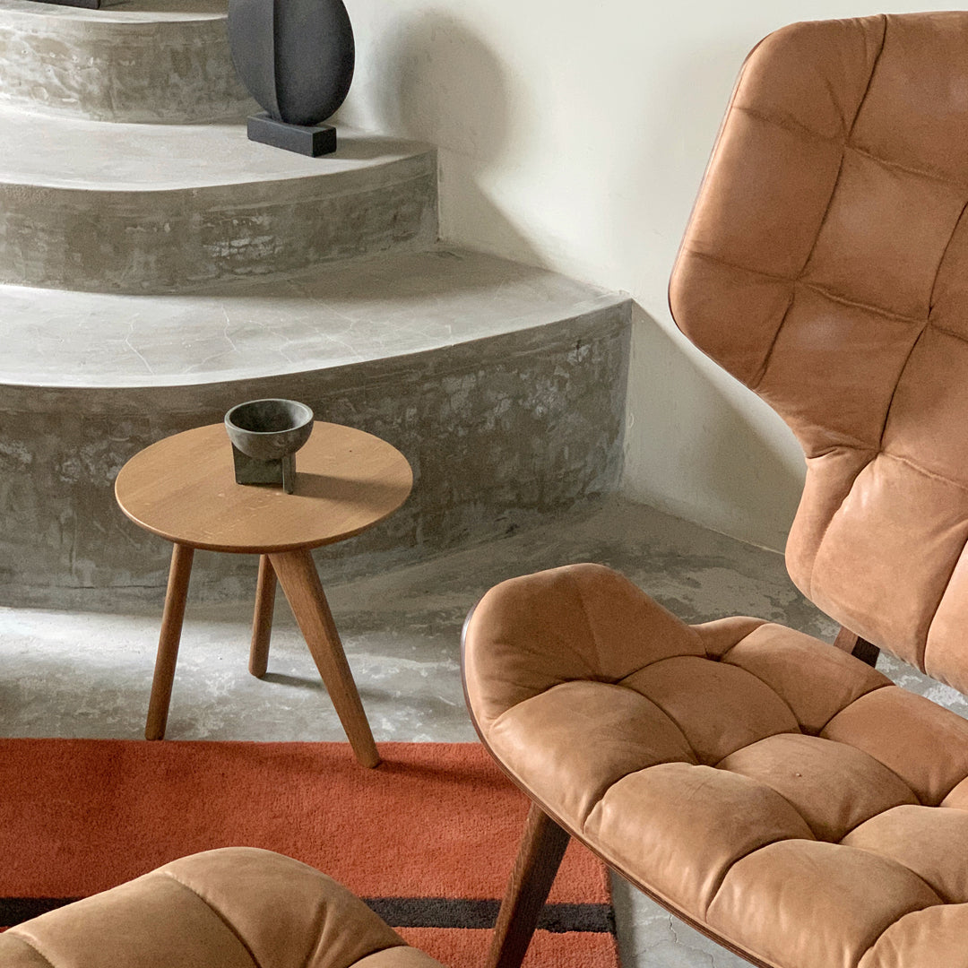 "Tan tufted chairs on a gray concrete staircase with a rust-colored rug and a minimalist round wooden table."