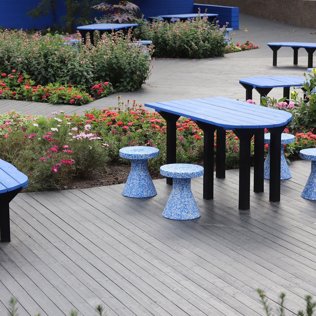 Blue patio table and stools with black legs, featuring floral pattern and vibrant garden background.