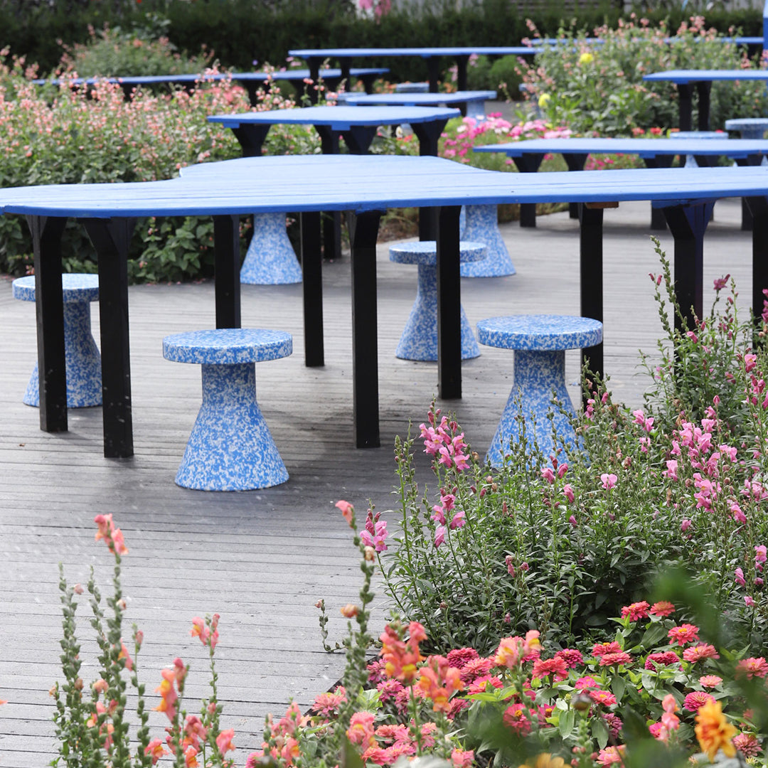 "Blue patterned tables and stools set against vibrant flower gardens in a colorful outdoor space."