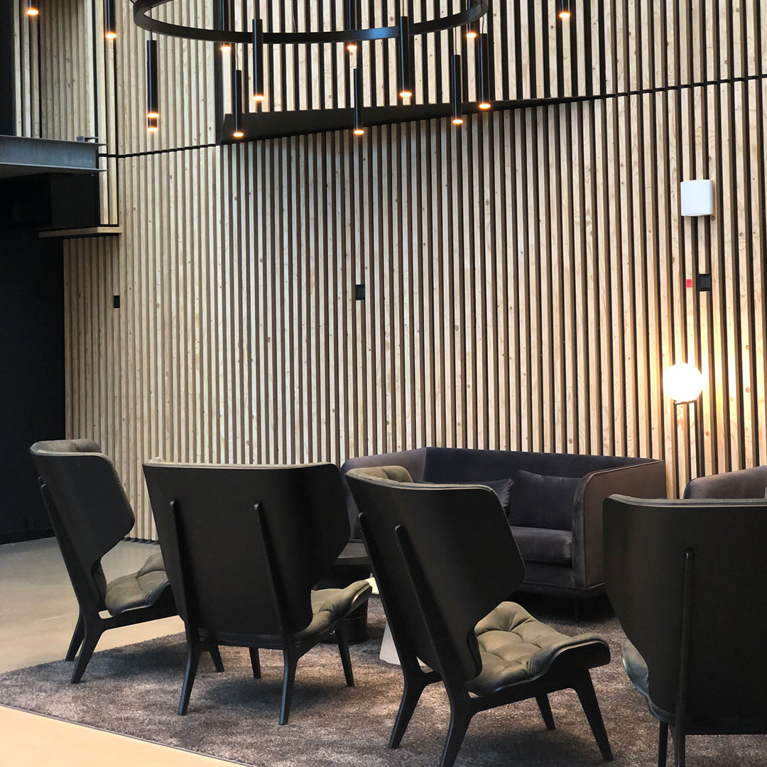 "Modern black armchairs with soft gray cushions against a textured wooden backdrop, illuminated by stylish lighting."