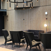 "Modern black armchairs with soft gray cushions against a textured wooden backdrop, illuminated by stylish lighting."