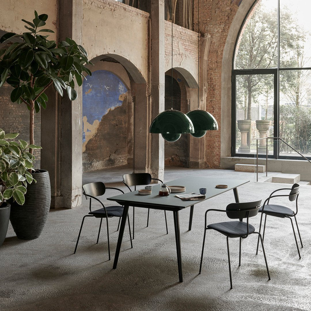 Modern dining set featuring black table, grey chairs, and green pendant lights against a natural, earthy backdrop.
