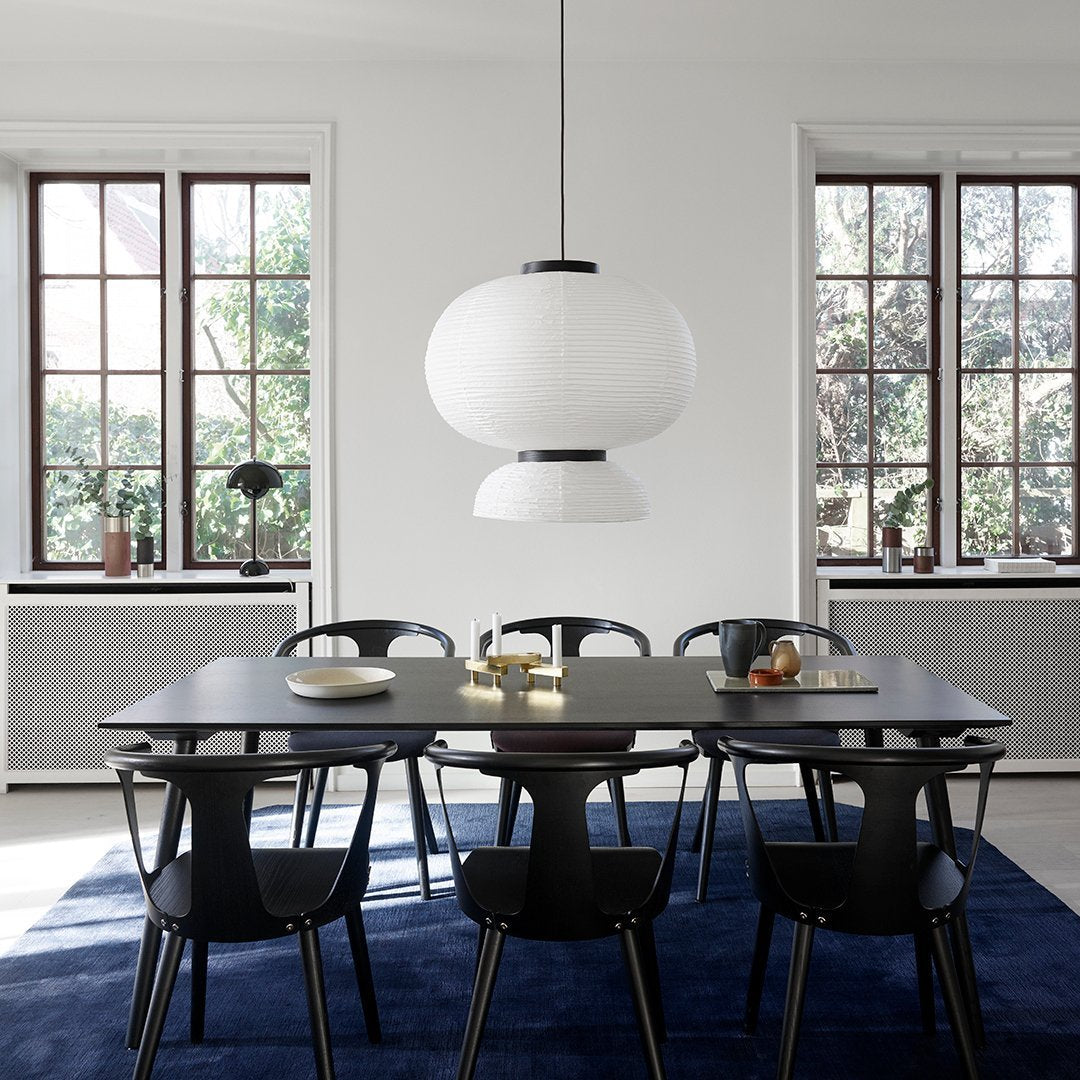 Modern dining room featuring a minimalist white pendant light, sleek black chairs, and a deep blue rug.