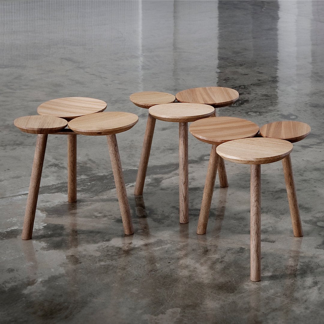 Natural wood stools with smooth circular tops and light wood tones, set against a polished concrete floor.