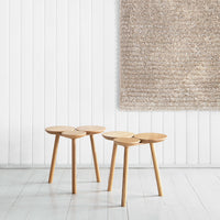 Natural wood stools with circular tops, paired with a textured beige rug on a white wall background.