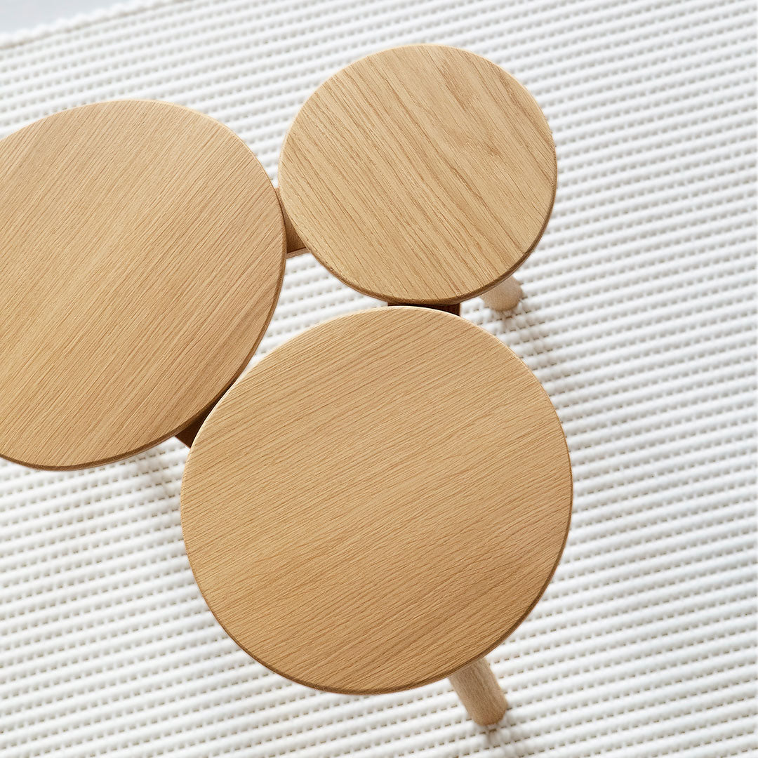 Natural wood circular side tables with smooth, light oak finishes, arranged on a textured cream rug.