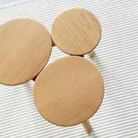 Natural wood circular side tables with smooth, light oak finishes, arranged on a textured cream rug.