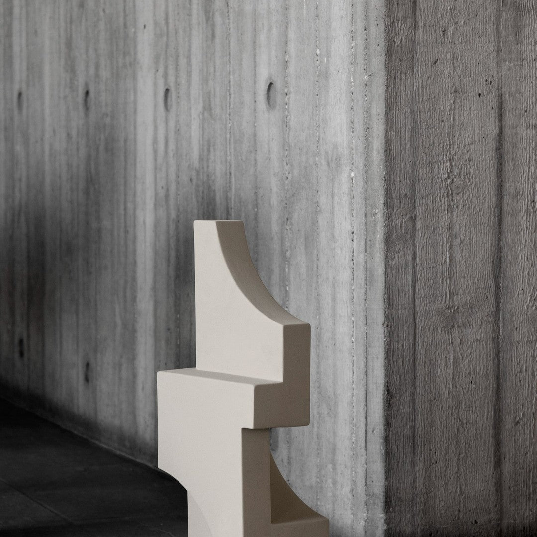 Cream geometric sculpture against a textured concrete wall, showcasing minimalistic design and elegant color contrast.
