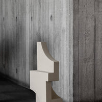 Cream geometric sculpture against a textured concrete wall, showcasing minimalistic design and elegant color contrast.
