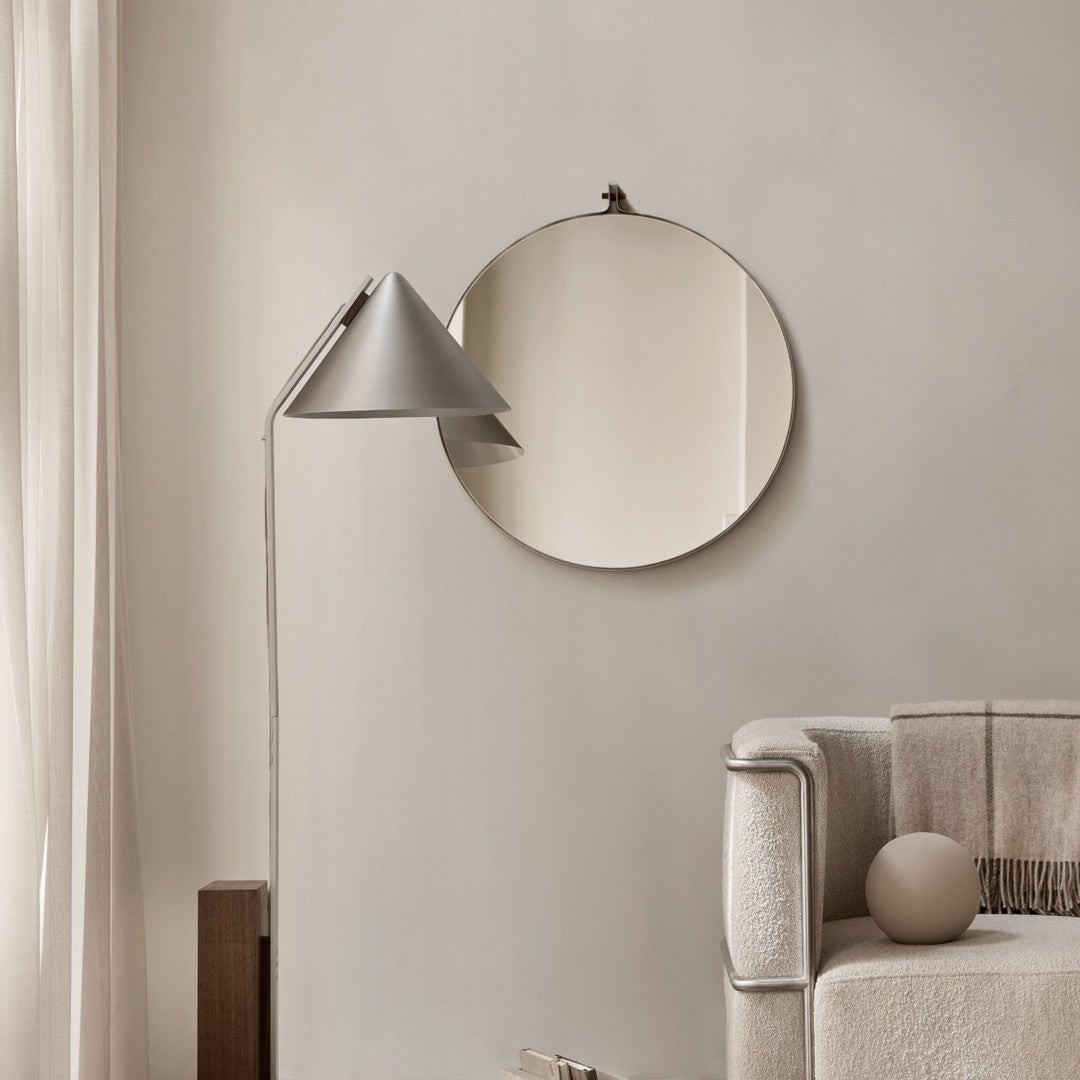 Minimalist gray circle mirror against a neutral wall, complemented by a sleek silver lamp and soft beige sofa.