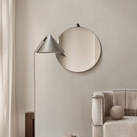 Minimalist gray circle mirror against a neutral wall, complemented by a sleek silver lamp and soft beige sofa.