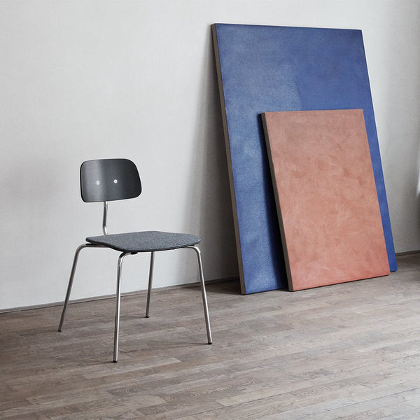 Gray chair with a minimalist design, set against blue and terracotta panels on a wood floor. Simple and modern color palette.