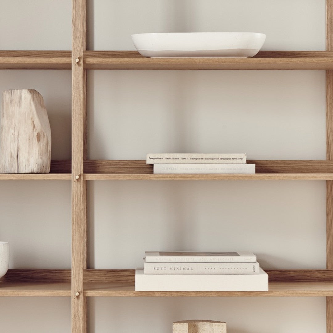 "Light wood shelving with neutral tones and simple, textured patterns, featuring white ceramics and stacked books."