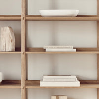 "Light wood shelving with neutral tones and simple, textured patterns, featuring white ceramics and stacked books."