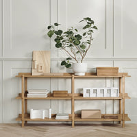 Natural wood shelving in light tones with white and beige decorative accents, accented by greenery. Modern minimalist design.