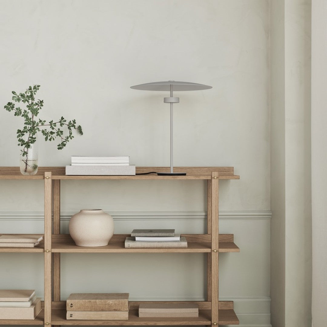 Stylish gray lamp on a natural wood shelf against a soft beige wall, complemented by a minimalist ceramic vase.