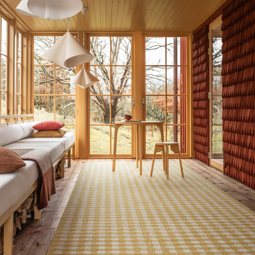"Yellow and white checkered area rug in a cozy, sunlit room with natural wood and earthy tones."