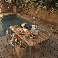 Wooden table with neutral tones, surrounded by vibrant purple flowers and earthy stone tiles, creating a serene outdoor vibe.