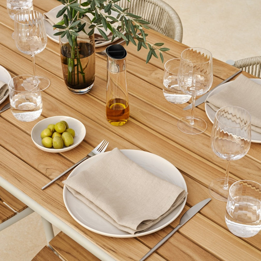 Neutral linen napkin on a white plate, paired with green olives on a wooden table setting with glassware.