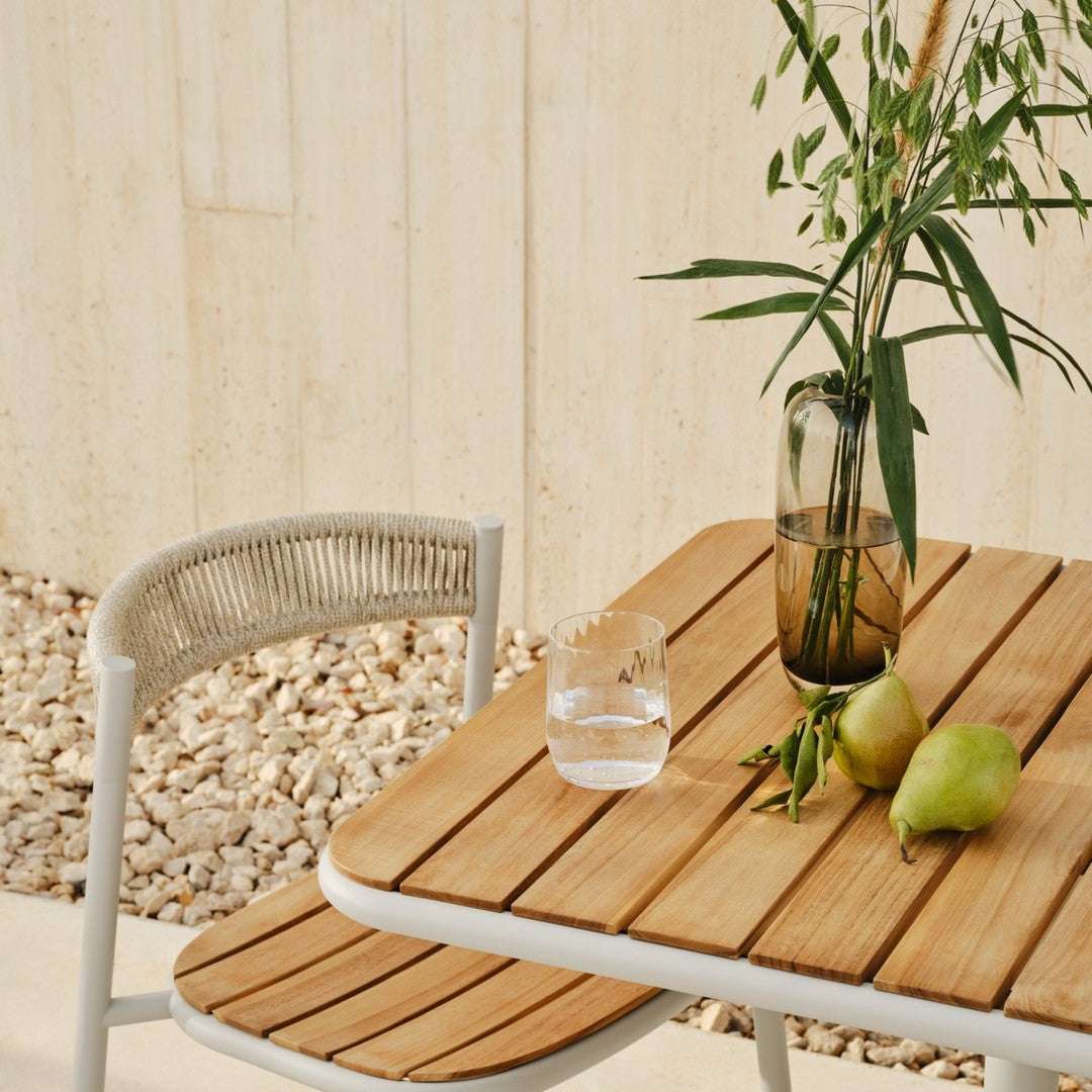 Wooden table with a natural finish, paired with a light gray woven chair, featuring fresh green pears and a clear glass vase.