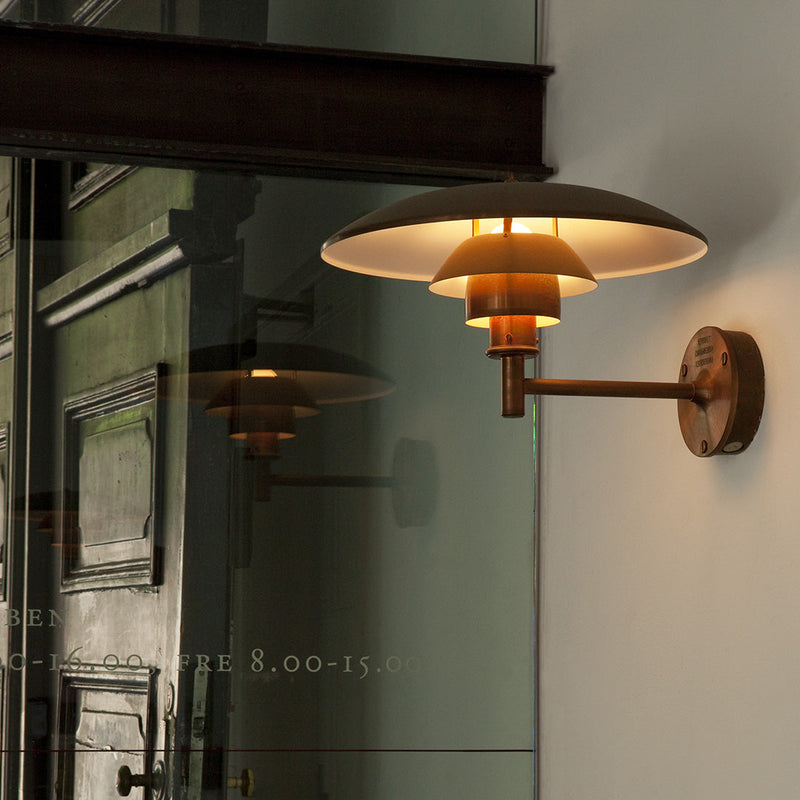 Bronze wall lamp with layered white and amber shades, reflecting elegant light against a minimalist backdrop.