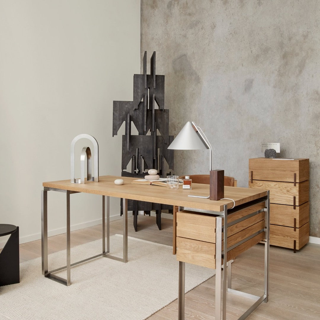 Natural wood desk with sleek silver legs, minimalist design, accented by gray wall and geometric black decor.