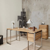 Natural wood desk with sleek silver legs, minimalist design, accented by gray wall and geometric black decor.