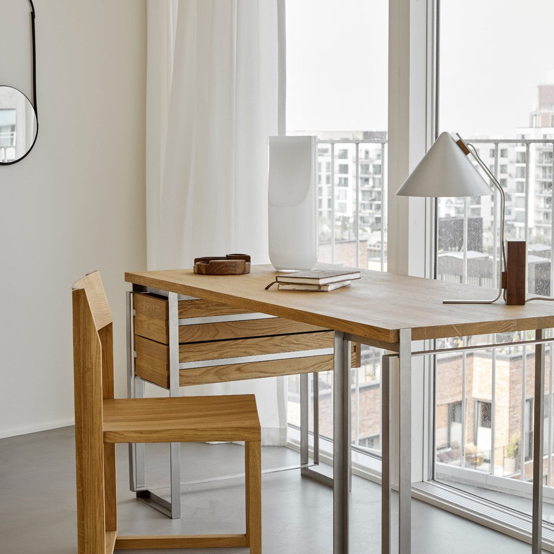 Modern wood desk and chair in natural tones, with sleek metal accents, in a light-filled, minimalistic setting.