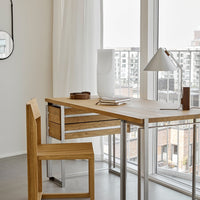 Modern wood desk and chair in natural tones, with sleek metal accents, in a light-filled, minimalistic setting.
