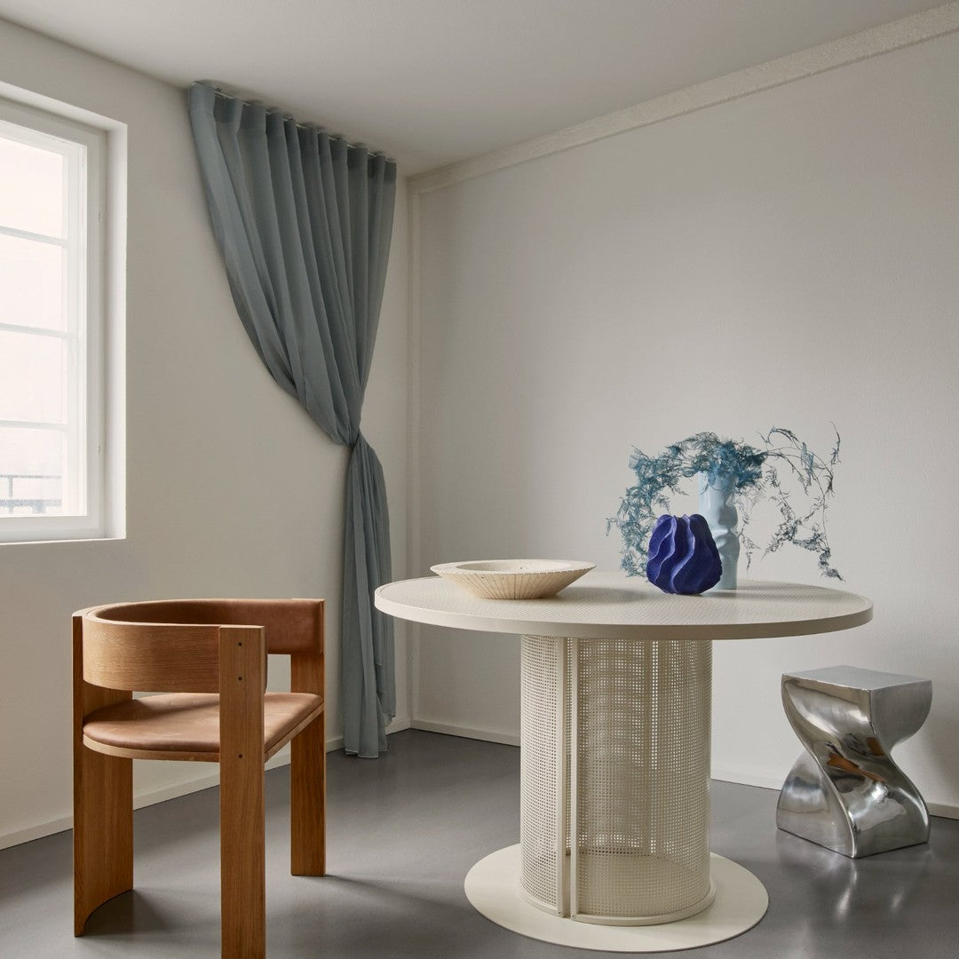 Modern beige round dining table adorned with a pale blue curtain and a unique blue decorative vase.