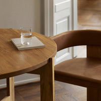 Wooden table with a warm, natural finish and a soft, tan leather chair; minimalistic design and earthy tones.