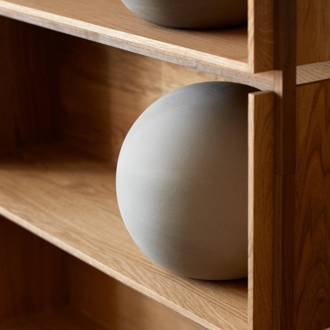 Light gray ceramic sphere on a wooden shelf, showcasing minimalist design and natural textures.