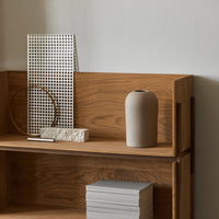 Minimalist wooden shelf showcasing a textured white grid, a beige vase, and stacked light gray books.
