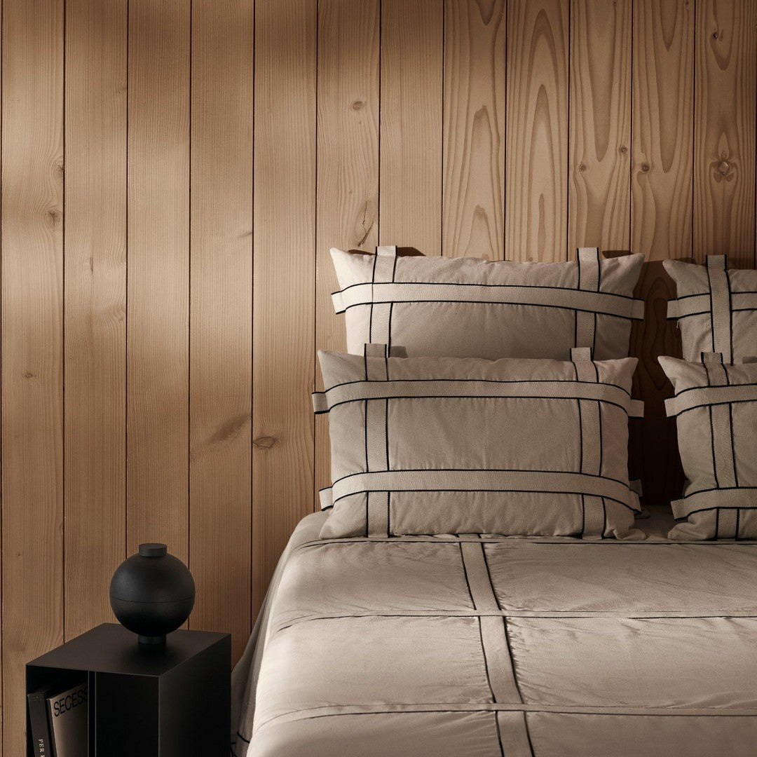 Beige bedding set featuring black grid patterns on pillows and quilt against a warm wooden backdrop.
