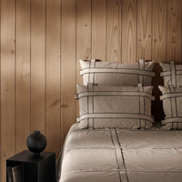 Beige bedding set featuring black grid patterns on pillows and quilt against a warm wooden backdrop.