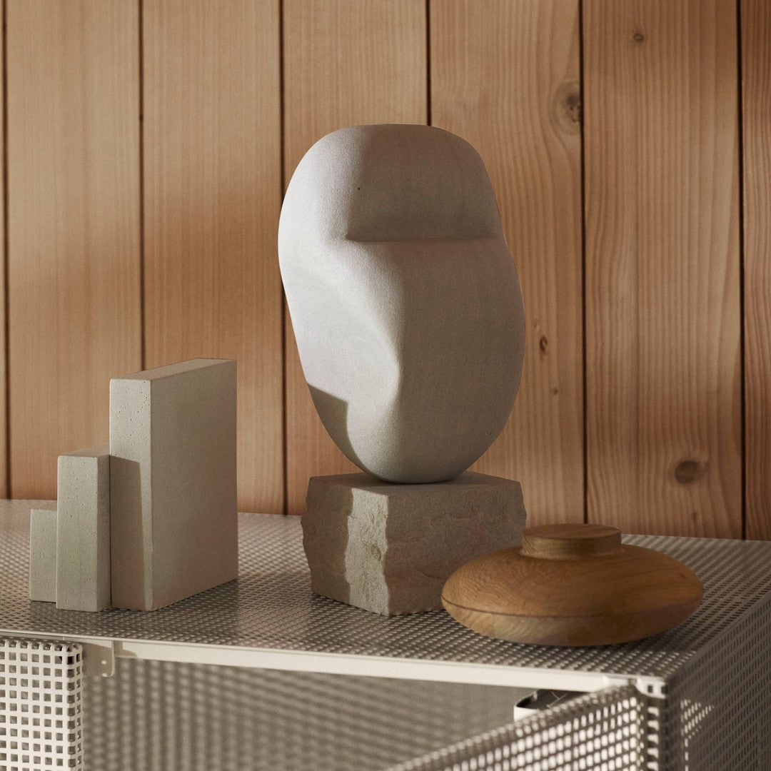 "Abstract stone sculpture in light gray and natural wood tones, set against a warm wooden backdrop."