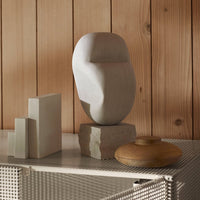 "Abstract stone sculpture in light gray and natural wood tones, set against a warm wooden backdrop."