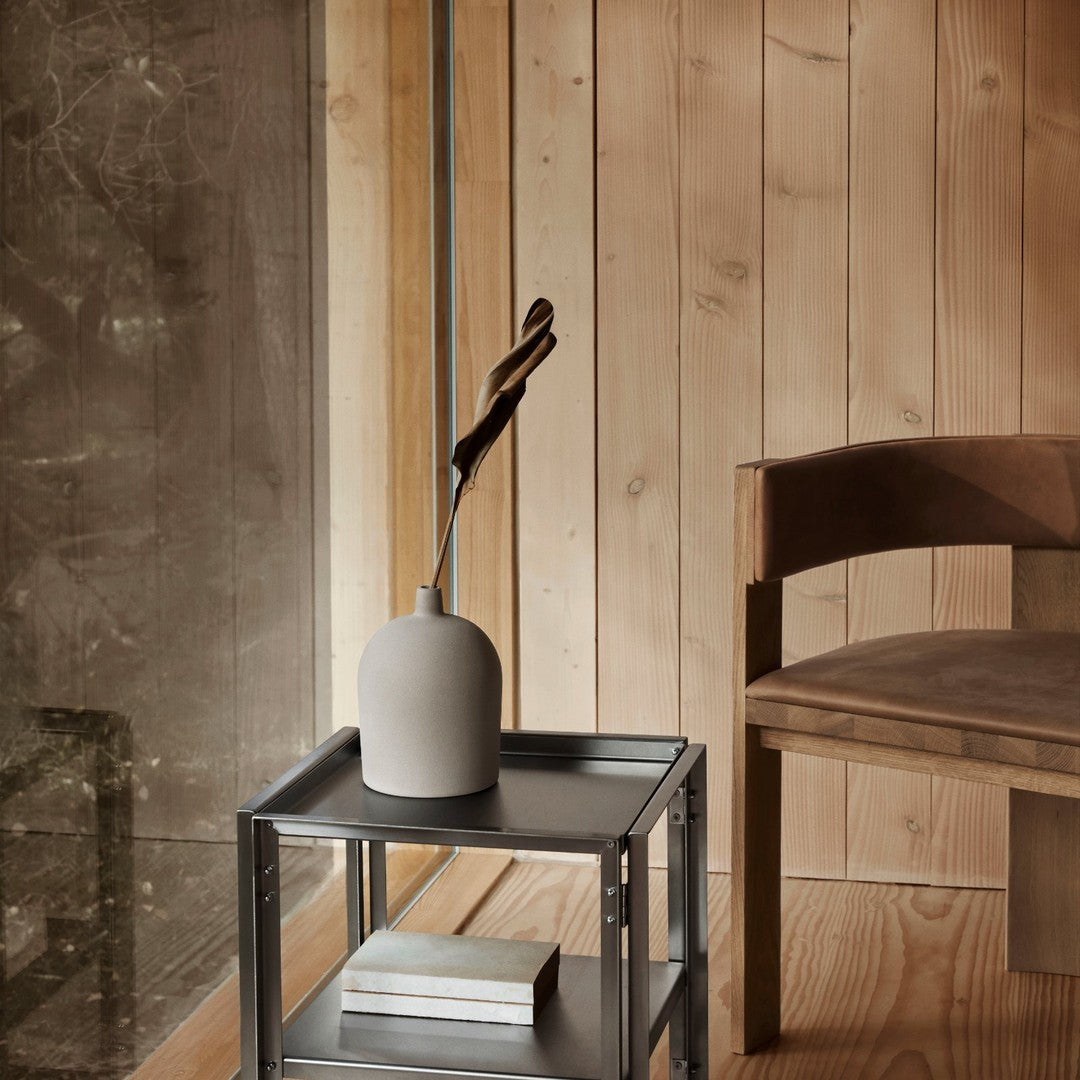 Gray ceramic vase with minimalist design on a sleek black metal table, surrounded by warm wood tones.