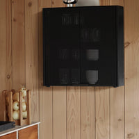 Black perforated wall cabinet with a sleek geometric pattern, mounted on wooden paneling.