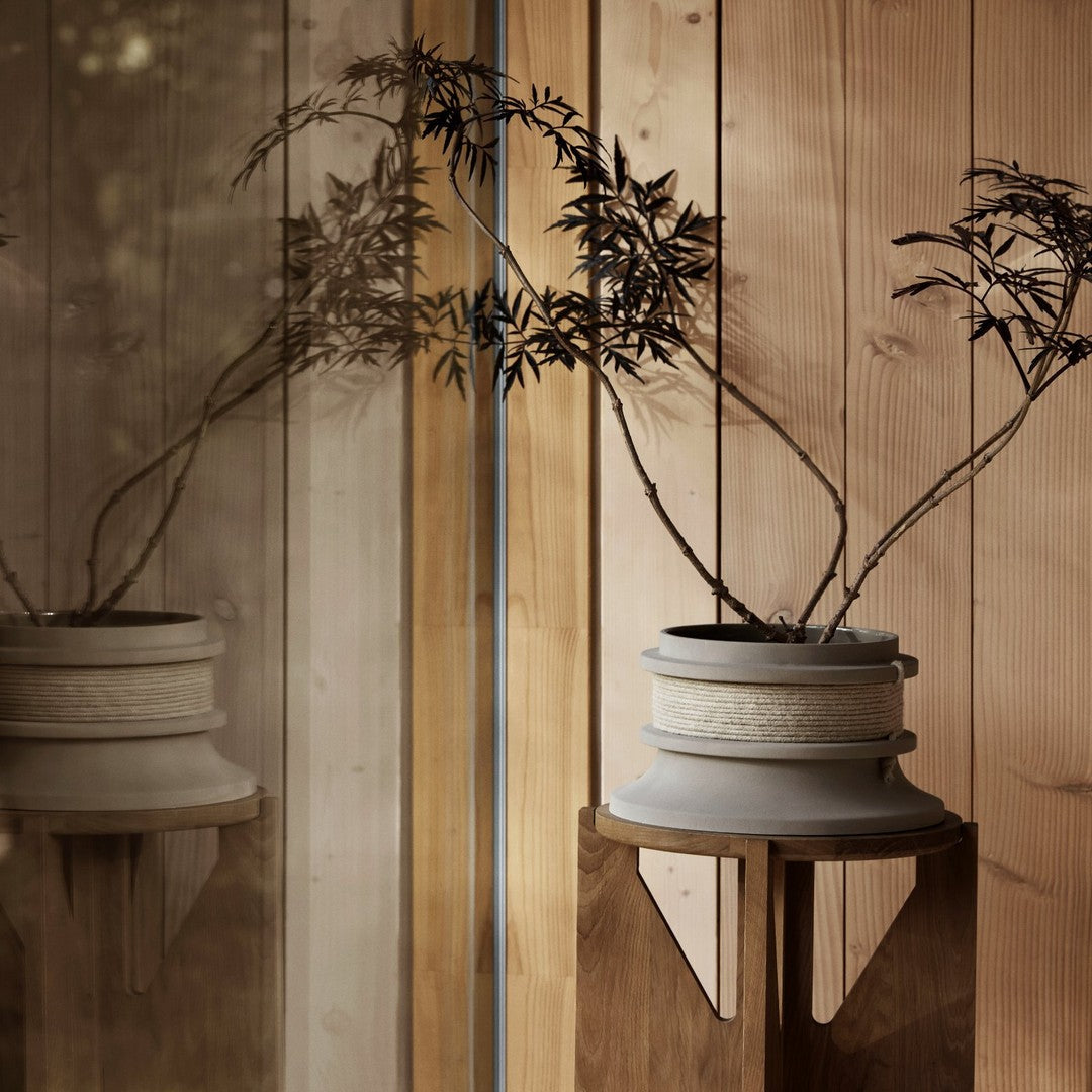 Ceramic planter in soft gray with textured details, featuring silhouetted plant branches against warm wooden backdrop.