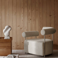 Beige modern chair with cylindrical arms, set against a warm wood panel background. Soft, minimalist design.